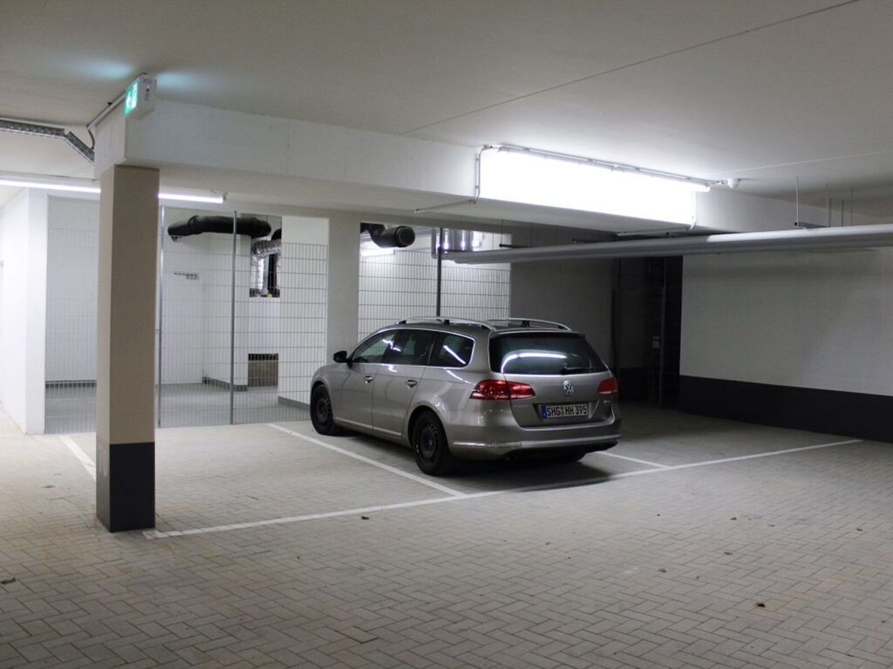 A parking garage with a silver station wagon parked in a spot.