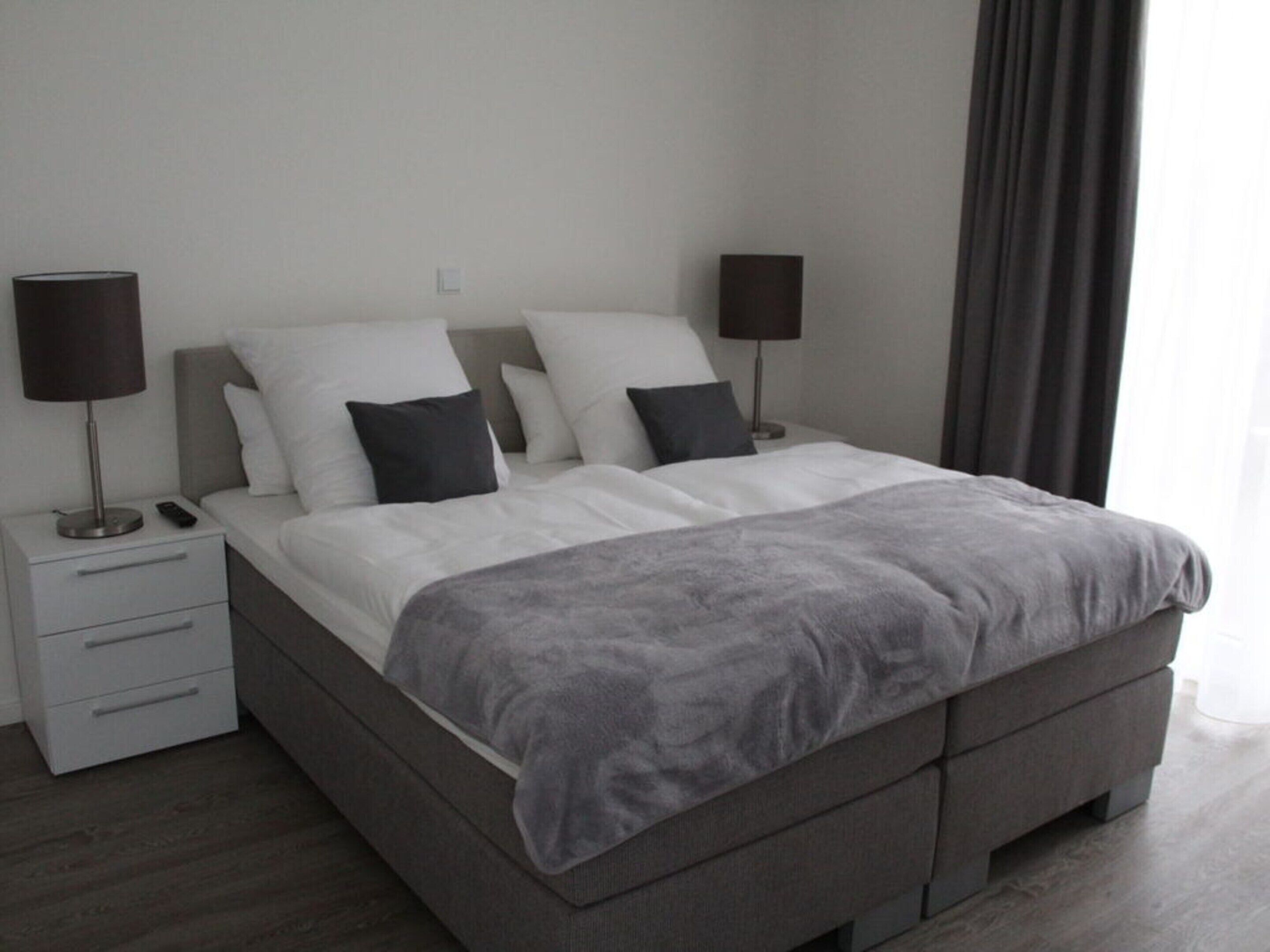 A modern bedroom with a large bed, two bedside tables, a lamp on each, and a grey blanket.