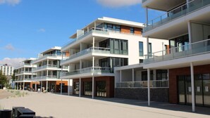 A modern multi-story residential building with balconies, large windows, and a paved walkway. - Seaside, South Cape Apartment D5 (Neustadt in Holstein)