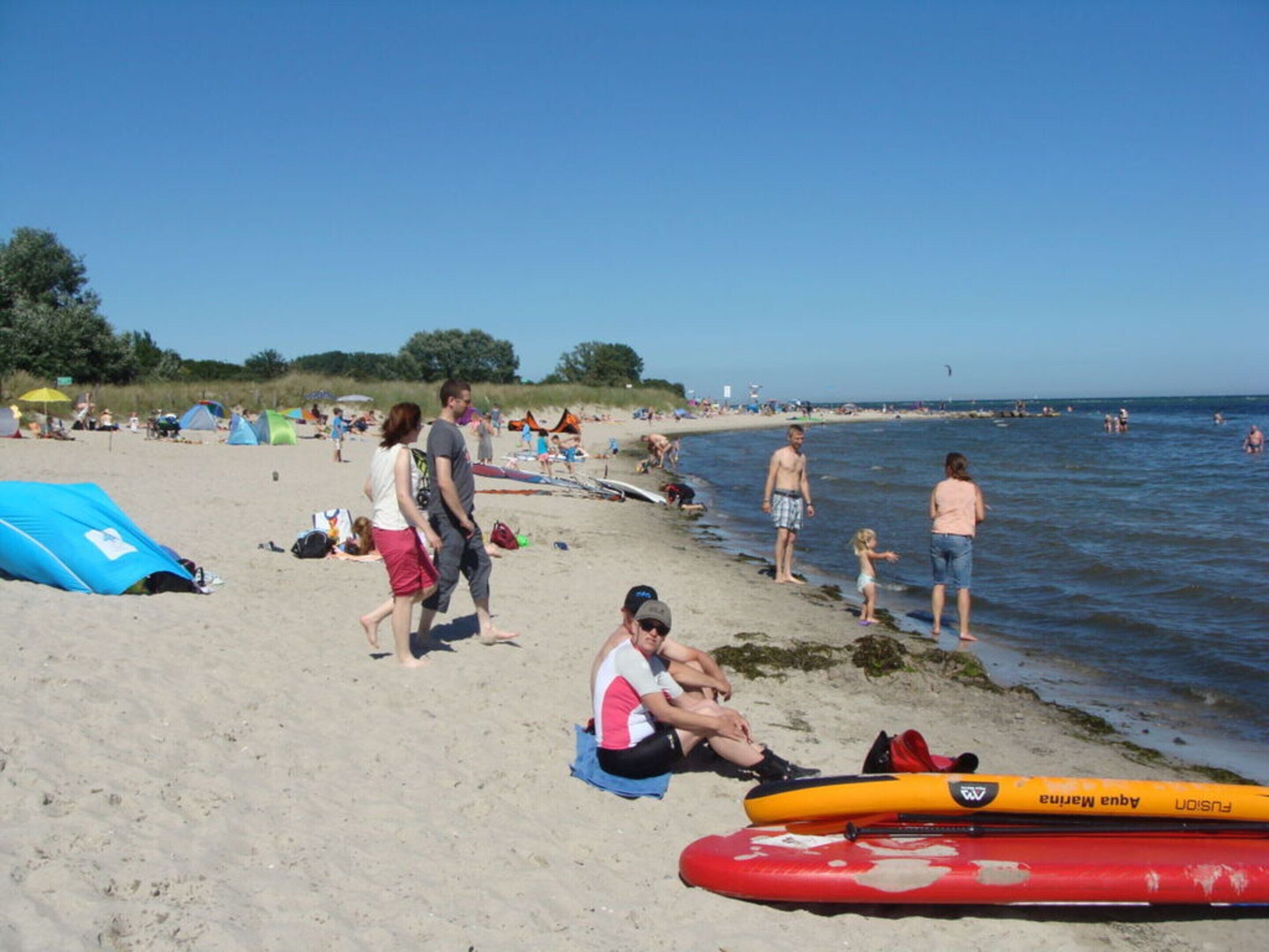 A beach with people, tents, and a red and yellow canoe.