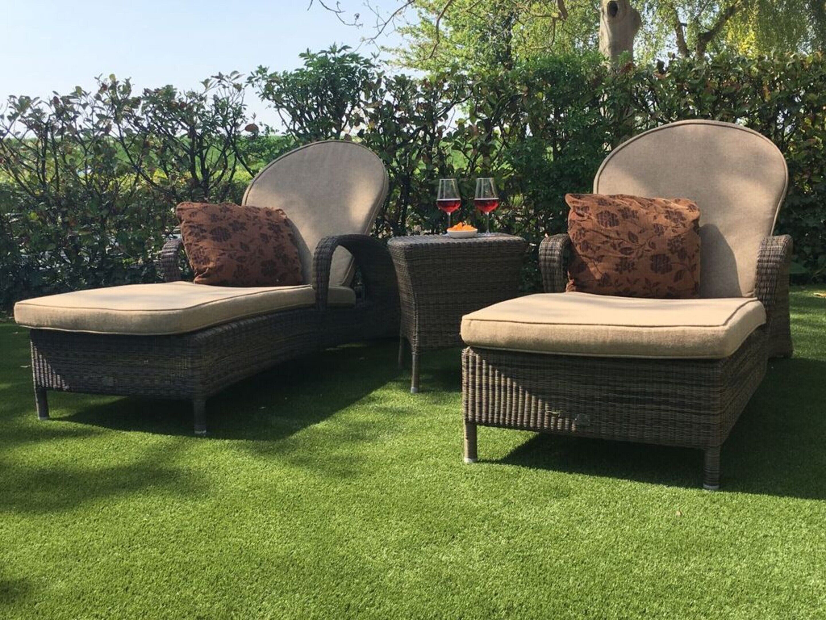Two wicker lounge chairs with cushions, a small table with two glasses of red wine, and a grassy lawn.