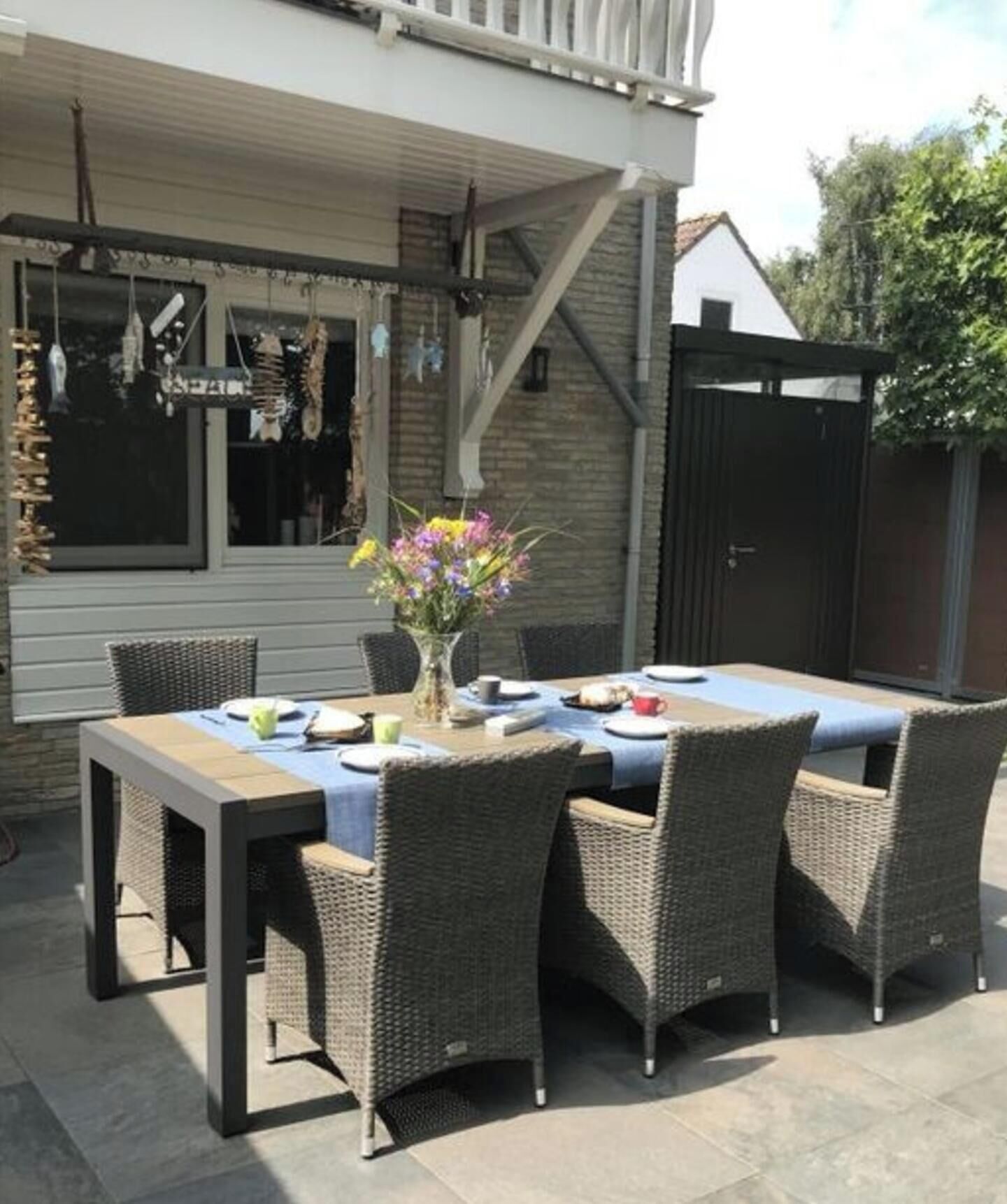 An outdoor patio with a table set for dining, surrounded by wicker chairs.