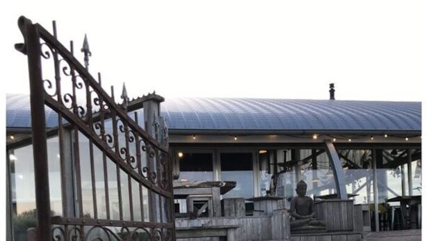 Une promenade en bois mène à un bâtiment doté d’une grille métallique.