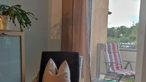Una habitación con una silla, una planta en maceta y vistas a un balcón con una silla a rayas.