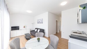 Ein modernes, minimalistisches Wohnzimmer mit einem grauen Sofa, einem weißen Couchtisch und einem Flachbildfernseher auf einer weißen Konsole.