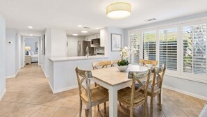A modern kitchen with white cabinets, a central island, and a dining area with a wooden table and chairs.