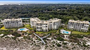 An aerial view of a resort with multiple buildings, a sandy beach, and a bridge connecting the structures.