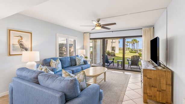 A living room with a sofa, coffee table, TV, and a balcony with outdoor furniture.