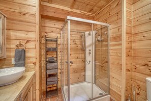 A wooden cabin bathroom with a glass-enclosed shower, a sink, and a towel rack.