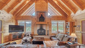 A log cabin interior with a fireplace, wooden furniture, and a television.
