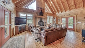 A spacious wooden cabin interior with a large living area, fireplace, television, and a cozy seating arrangement.