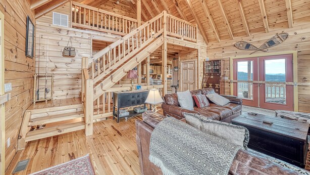 A wooden cabin interior with a staircase leading to a loft, a living area with a sofa and coffee table, and a fireplace.