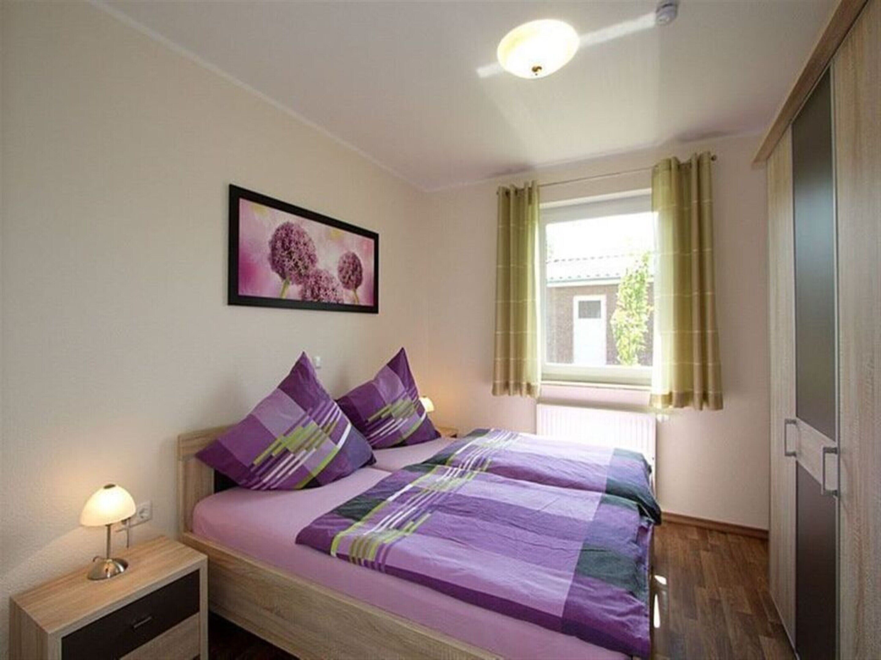 Une chambre avec deux lits, une table de chevet avec une lampe, une fenêtre avec des rideaux et un tableau encadré au mur.