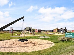 A playground with swings and a slide, surrounded by small buildings and a sign that reads "Helmklink Havn". - 5 Person Holiday Home in Ulfborg (Ulfborg)