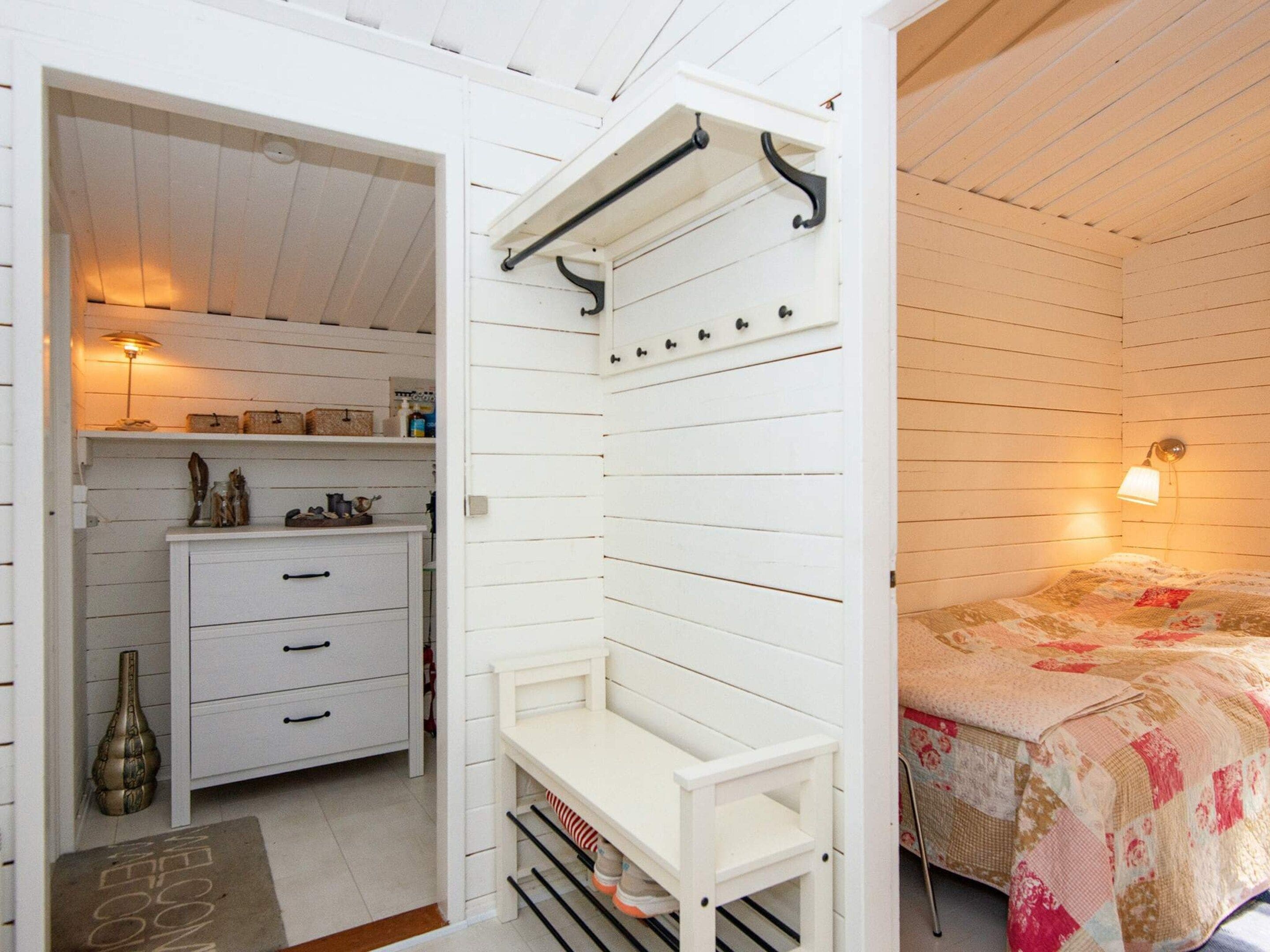 A bedroom with a bed, a bedside table, a nightstand, a wardrobe, and a hanging rack.