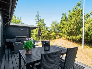 An outdoor patio with a table and chairs, surrounded by trees and a wooden building. - 5 Person Holiday Home in Ulfborg (Ulfborg)