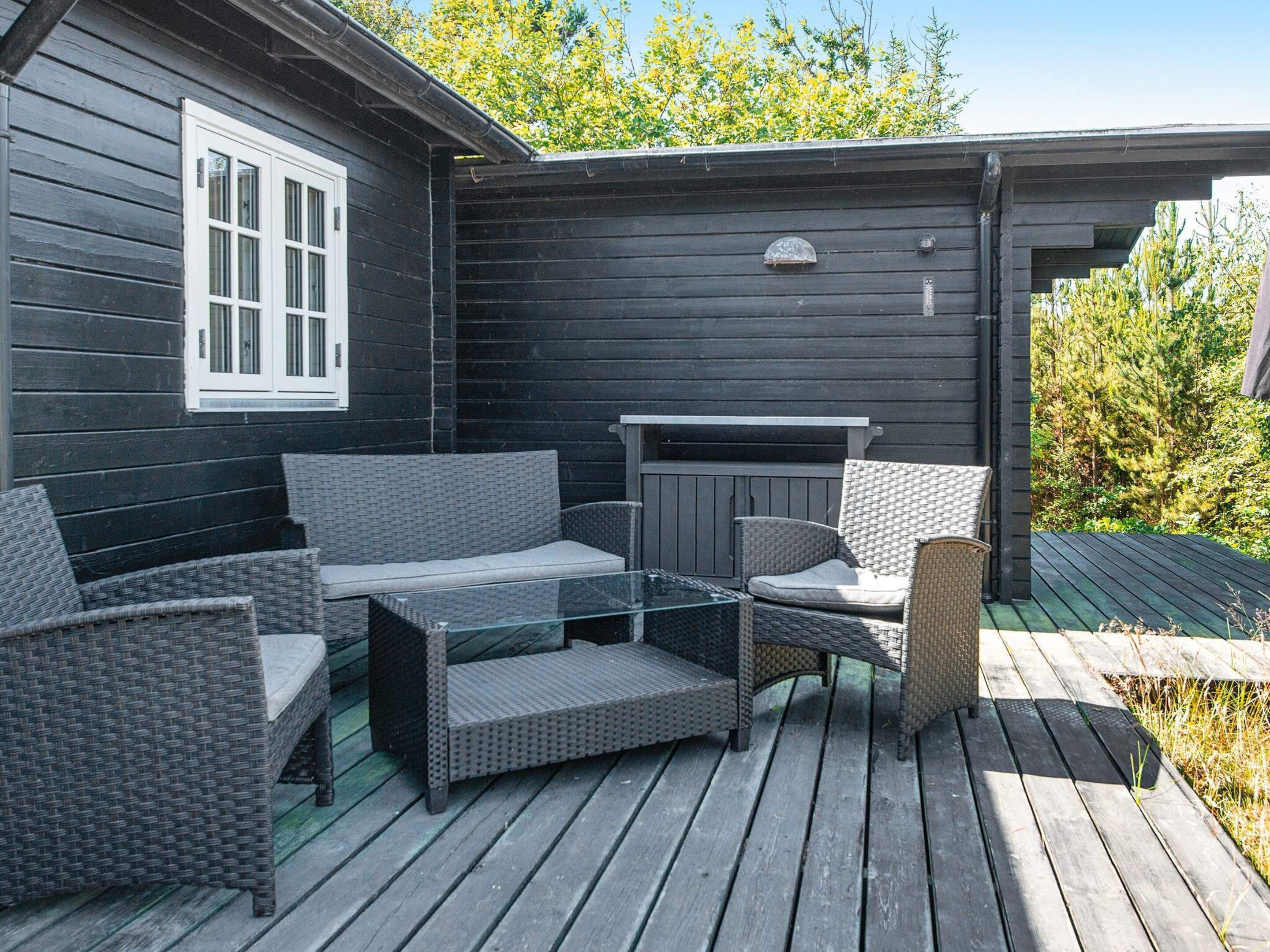 An outdoor patio with wicker furniture, a glass-top table, and a fireplace.