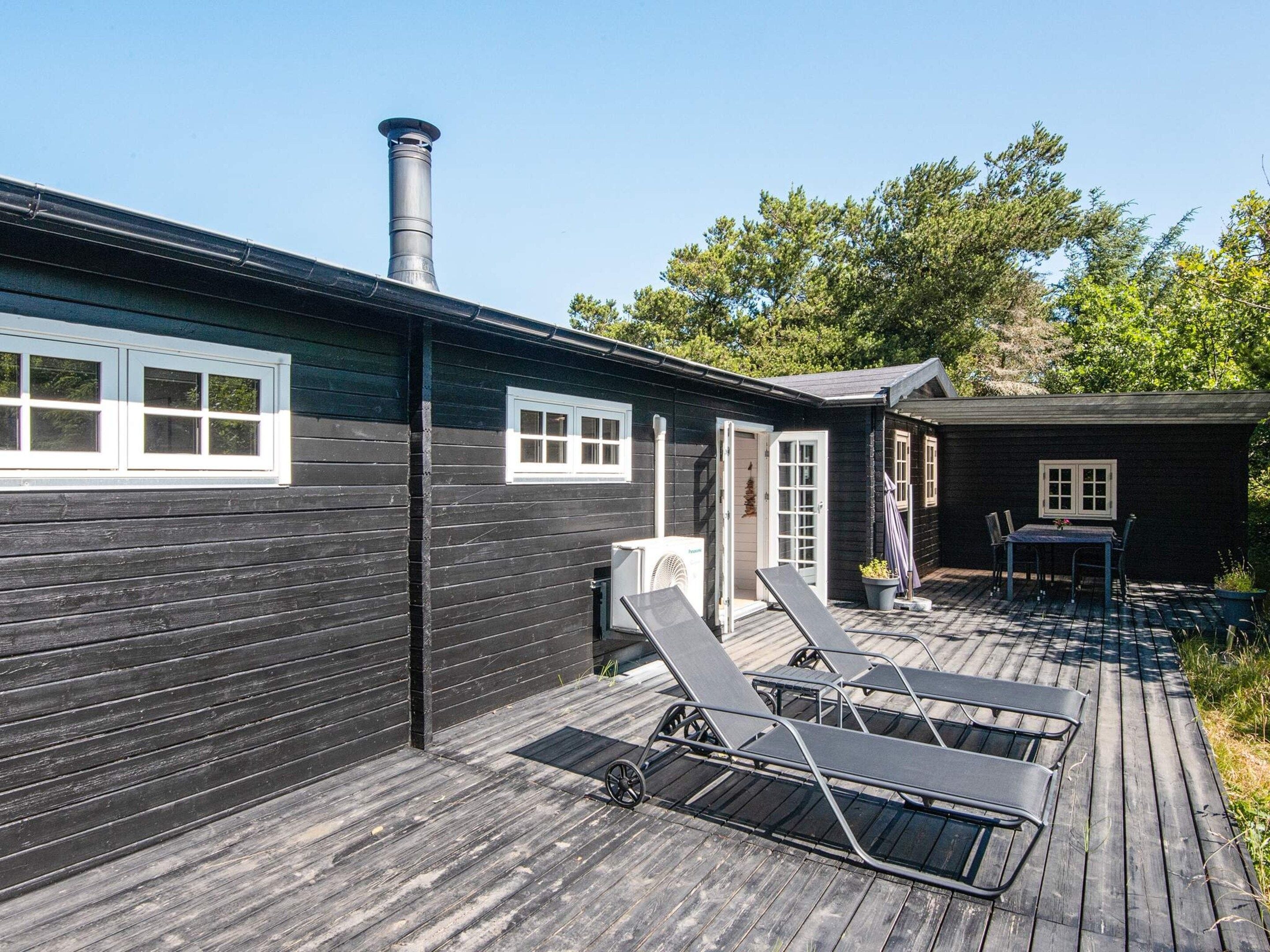 A wooden house with a covered patio, a chimney, and a small attached structure with a table and chairs.