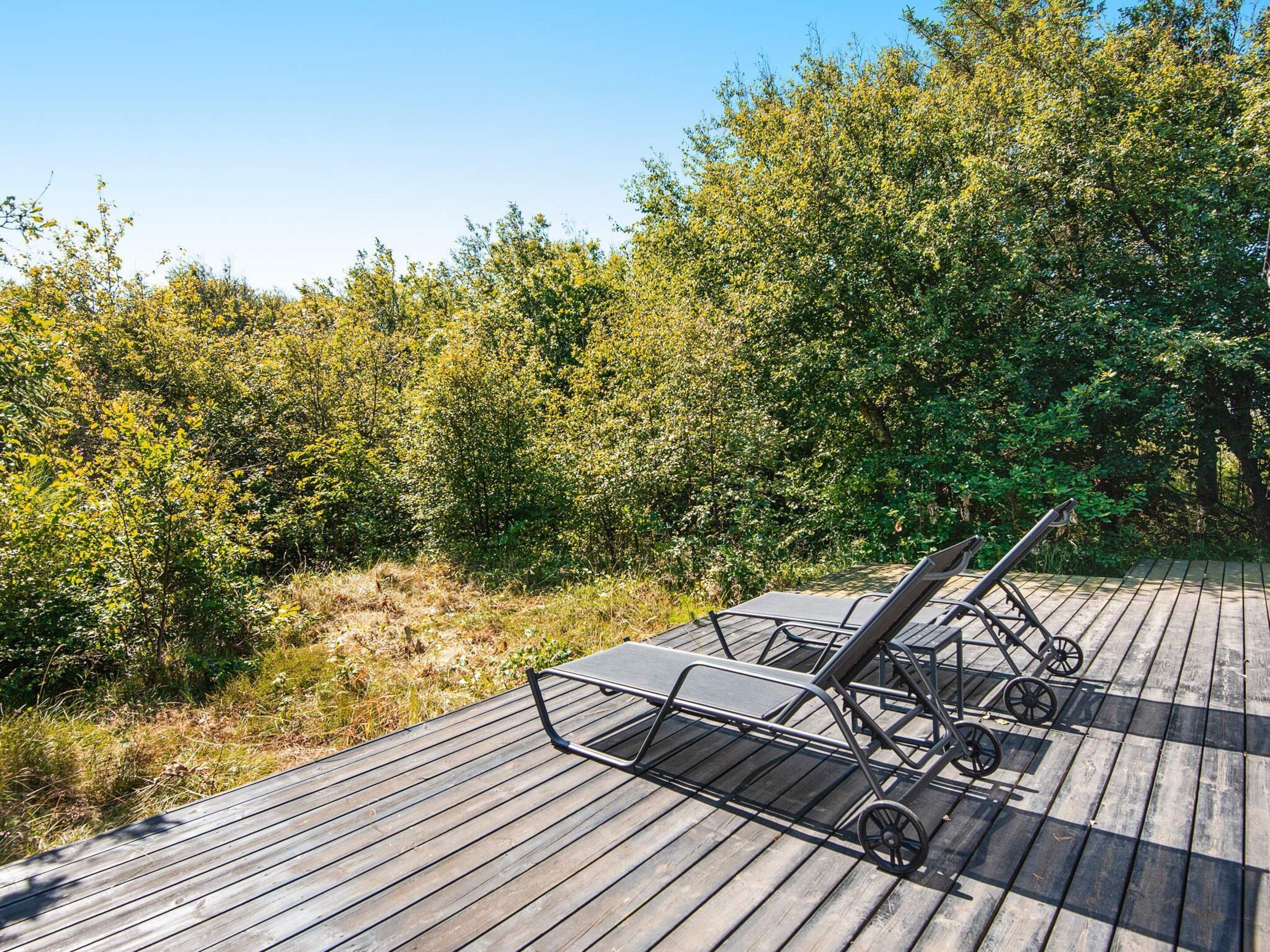 Une terrasse en bois avec deux chaises longues et une petite table, entourée d’une végétation luxuriante.