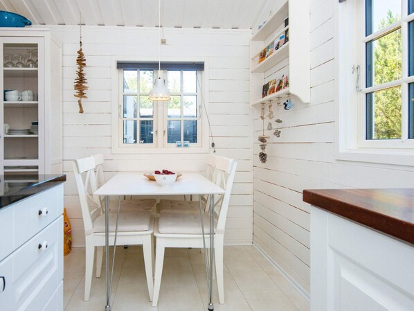 A kitchen with white cabinetry, a dining table with chairs, a hanging light fixture, and a window with a view of greenery outside.