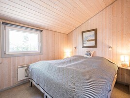 Un dormitorio con cama, ventana, radiador y lámpara fijada a la pared.