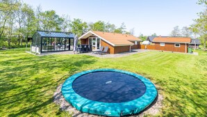 Een achtertuin met een trampolaan, een glazen kas en een houten hutje.