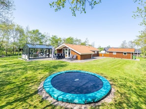 A backyard with a trampoline, a glass greenhouse, and a wooden cabin. - 4 Person Holiday Home in Hemmet (Hemmet)