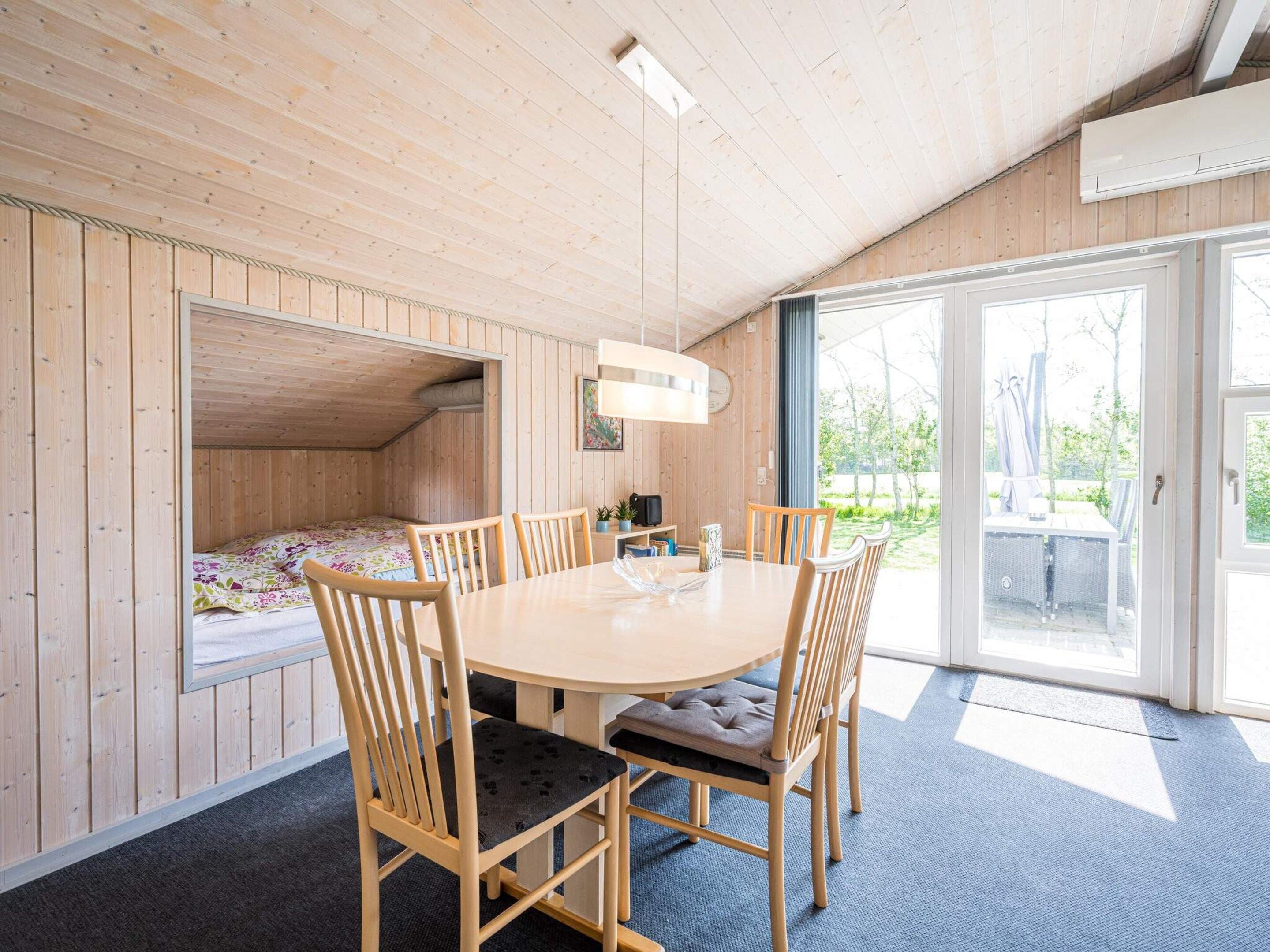 Een kamer met houten inrichting, een ronde tafel met stoelen, een bed met een kleurrijk sprei en een groot raam.