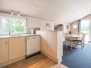 A modern kitchen with wooden cabinets, a dishwasher, and a dining area with a table and chairs. - 4 Person Holiday Home in Hemmet (Hemmet)