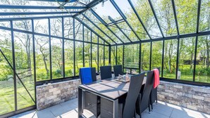 Een glazen terras met een tafel en stoelen, een bakstenen muur en uitzicht op groen.