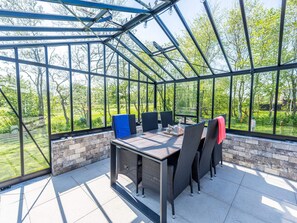 A glass-enclosed patio with a table and chairs, a brick wall, and a view of greenery. - 4 Person Holiday Home in Hemmet (Hemmet)