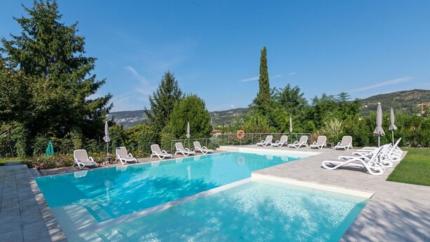 A rectangular swimming pool with clear blue water, surrounded by white lounge chairs and umbrellas. - Comfortable Apartment in Garda With Swimming Pool (Garda)