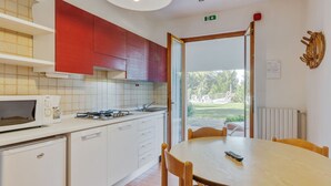 A modern kitchen with white cabinets, a microwave, and a stove. There is a dining table with chairs and a remote control on it. - Comfortable Apartment in Garda With Swimming Pool (Garda)