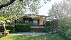 A two-story house with a balcony, surrounded by a well-maintained garden and a wooden fence. - Comfortable Apartment in Garda With Swimming Pool (Garda)