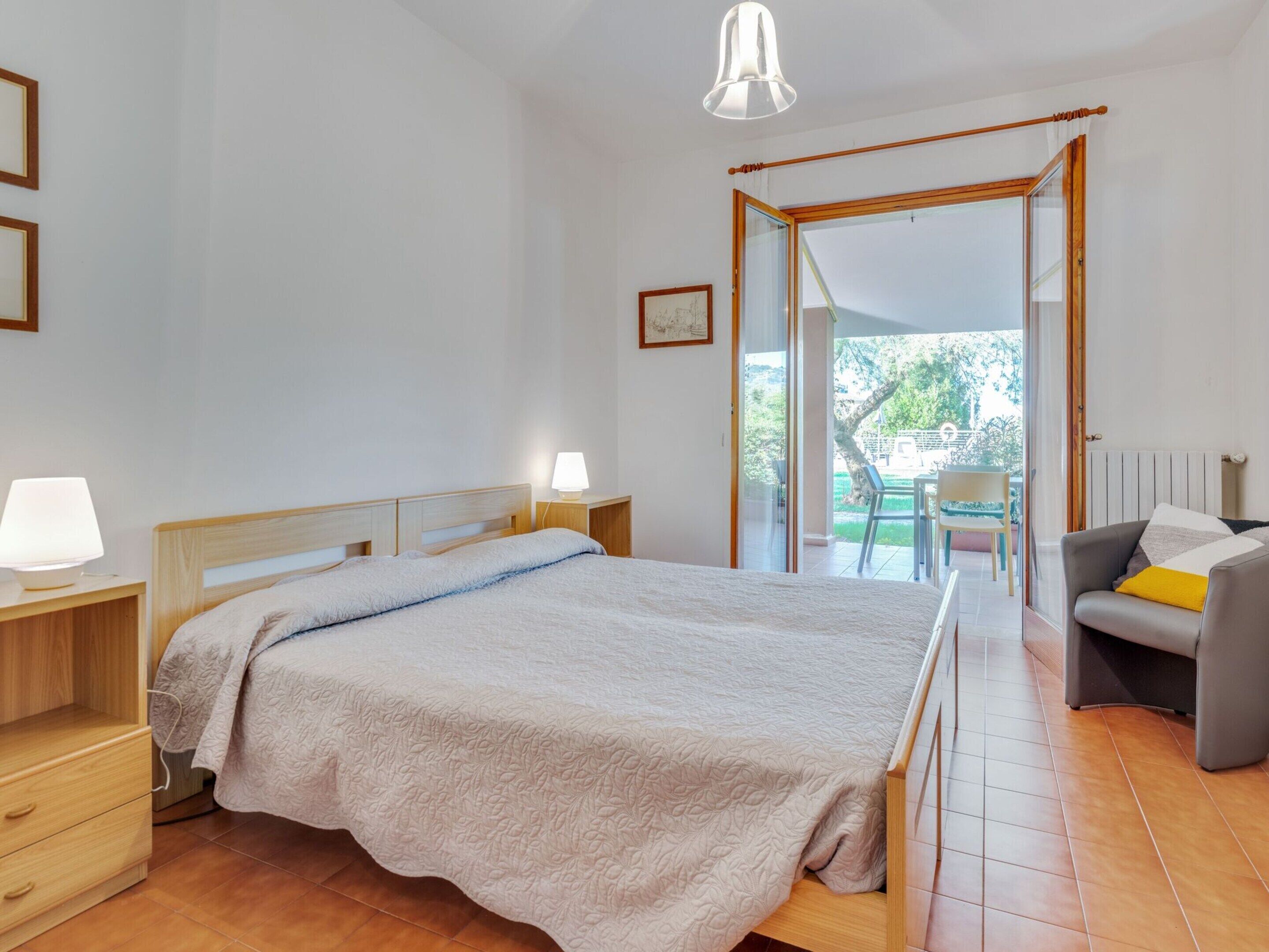 A bedroom with a bed, bedside tables, a lamp, a chair, and a view of the outdoors.
