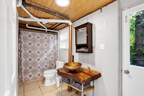 A bathroom with a wooden vanity, a toilet, a shower curtain, and a window with a view of trees.