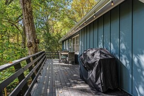 A covered deck with a table and chairs, surrounded by trees.
