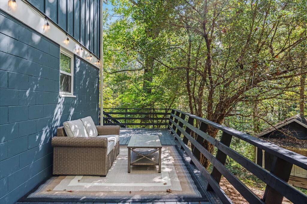 A covered outdoor area with a sofa and table, surrounded by a wooden deck and trees.