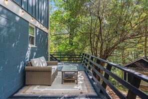 A covered outdoor area with a sofa and table, surrounded by a wooden deck and trees.