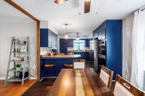 A modern kitchen with blue cabinets, a wooden dining table, and a ladder shelf.