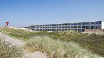 Un edificio moderno con techo plano y ventanas amplias, rodeado de dunas de arena y hierba.