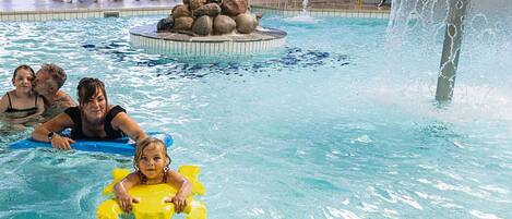 A pool with a water fountain, lounge chairs, and a rock feature.