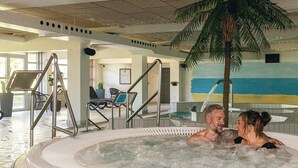 A hot tub with two people, indoor seating area, and a palm tree. - 8 Person Holiday Park Home in Blokhus (Blokhus)