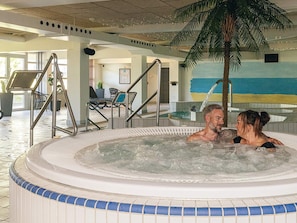 Een hottub met betegelde rand, een binnenzithoek met stoelen en een palmboom.