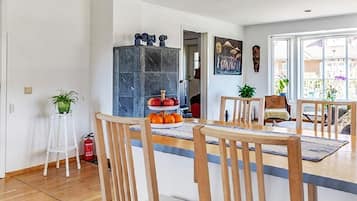 A dining area with a wooden table and chairs, a fruit display, and a view of the outdoors through large windows.
