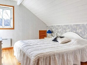 A bedroom with a sloped ceiling, a bed with a white headboard, a nightstand with a lamp, and a window with a view of trees. - 4 Person Holiday Home in Motala (Motala)