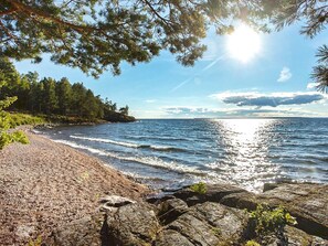 A beach with a rocky shoreline, trees, and a clear sky. - 4 Person Holiday Home in Motala (Motala)