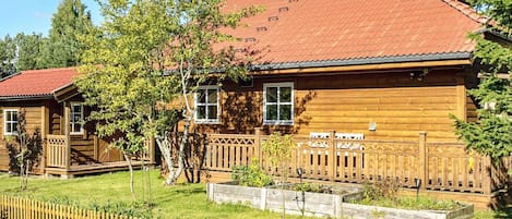 En træhytte med rødt tegltag, en træterrasse og en indhegnet have.