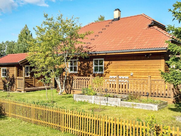 A wooden cabin with a red-tiled roof, a wooden deck, and a fenced yard. - 4 Person Holiday Home in Motala (Motala)