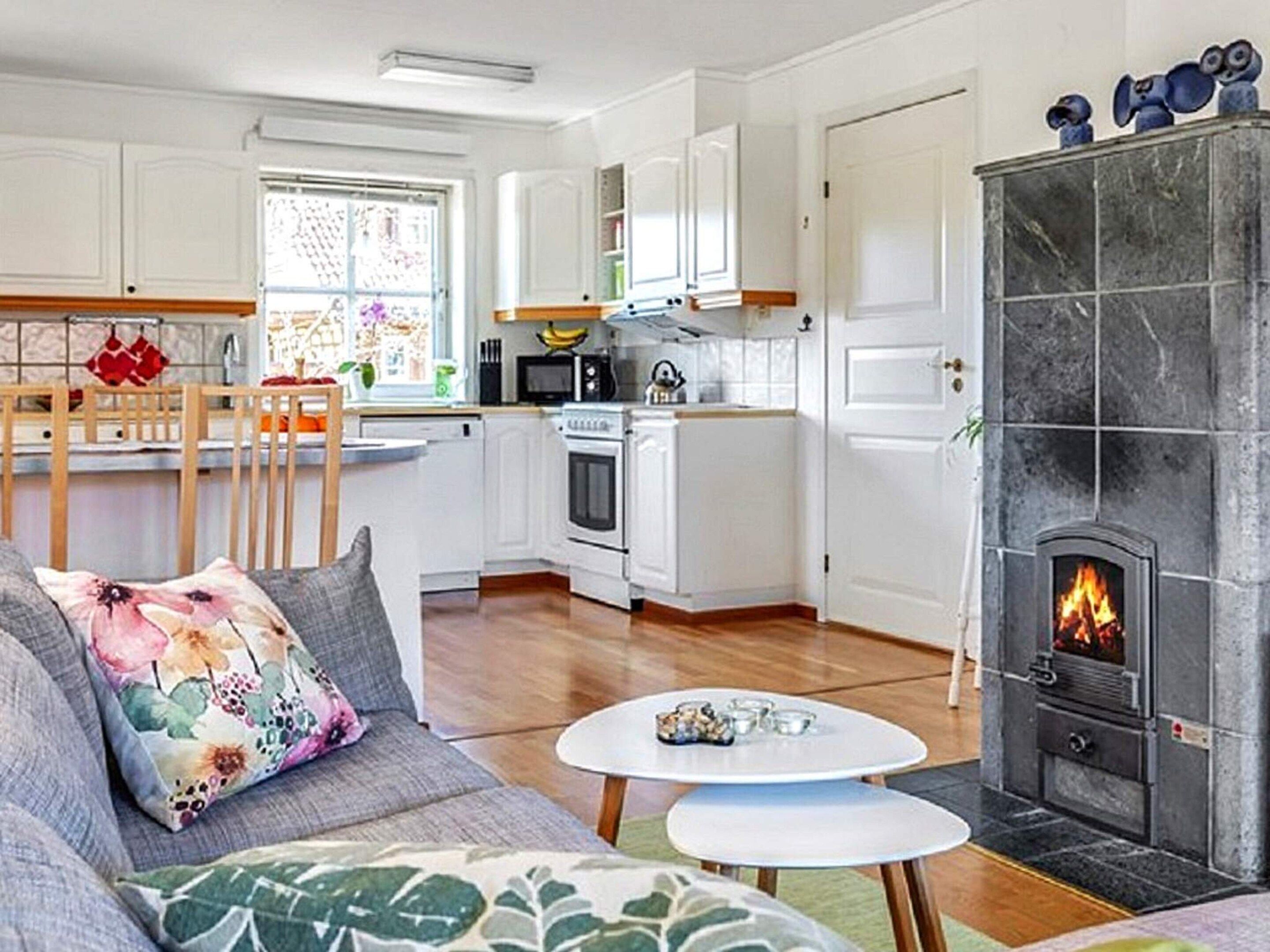 A modern kitchen with white cabinets, a dining area with a wooden table, and a fireplace with a visible fire.